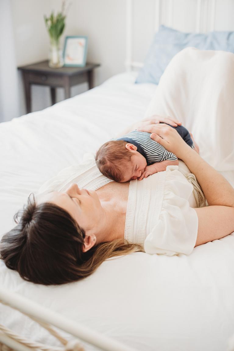 A young mom is holding a newborn baby on her chest during in-home lifestyle photography session by Toronto newborn photographer.